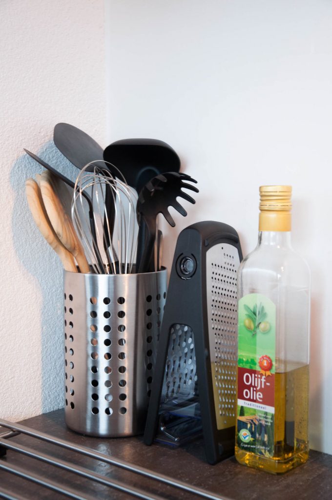 A picture of kitchen utensils, a cheese grater, and a bottle of olive oil next to a stove. First Kitchen Essentials for Your New Apartment