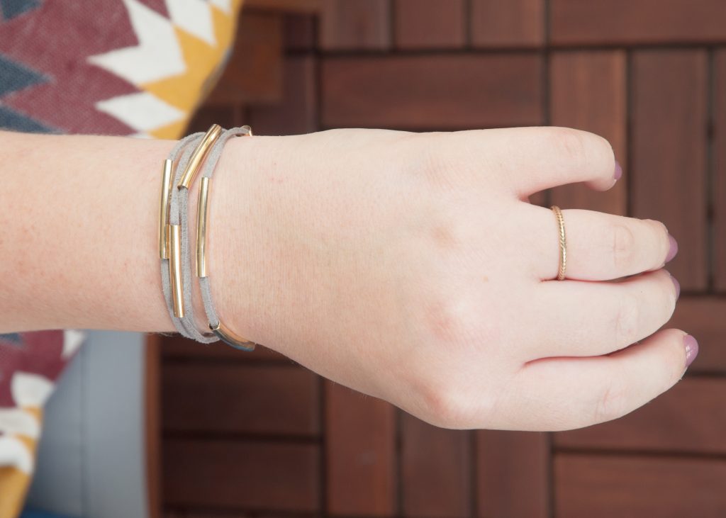 3 Easy DIY Bracelets You'll Actually Want to Wear. Image Description: A wrist featuring a gray wrap bracelet with gold beads, and wearing a gold ring.