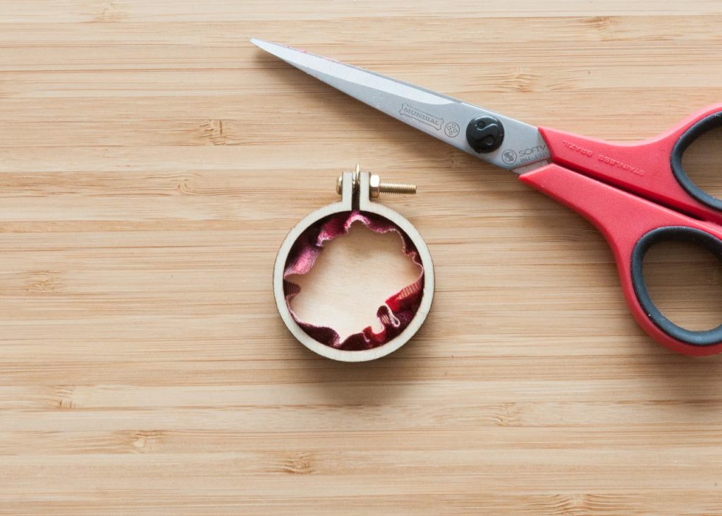 How to Make No-Sew Mini Embroidery Hoop Necklaces.Image description: Back of a mini embroidery hoop and a pair of scissors.