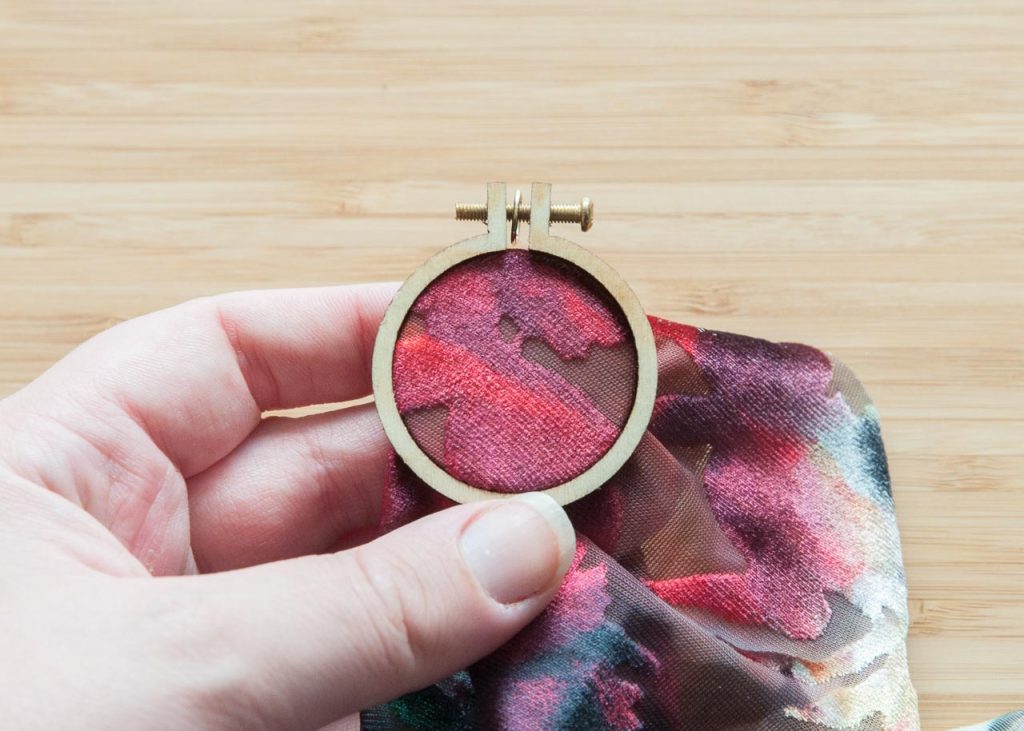 How to Make No-Sew Mini Embroidery Hoop Necklaces. Pictured: A mini embroidery hoop on red velvet fabric.